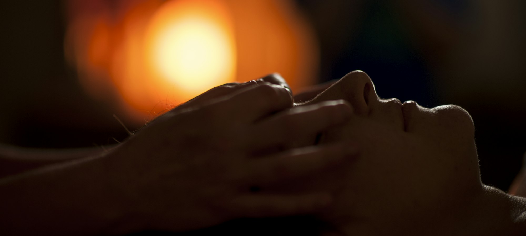 Hands gently massaging a client's face in warm, low light
