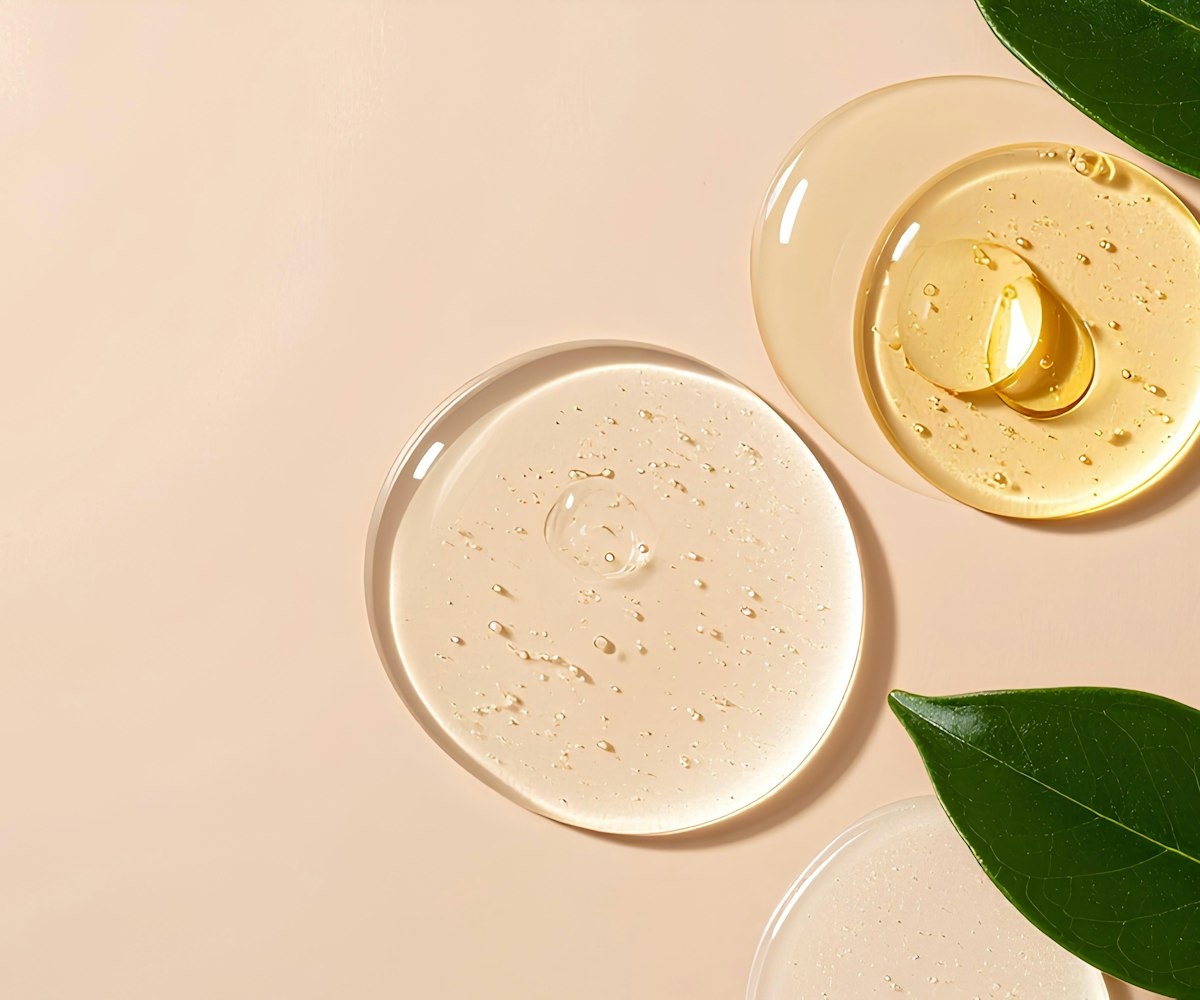 Drops of clear and golden serum with green leaves on a soft peach background